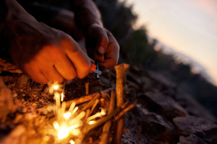 Nahaufnahme einer Person, die mit Feuerstein und Stahlwolle ein Feuer macht