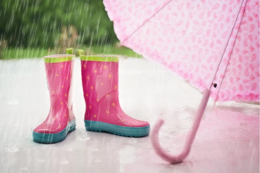 Süße rosa Stiefel und Regenschirm im Regen