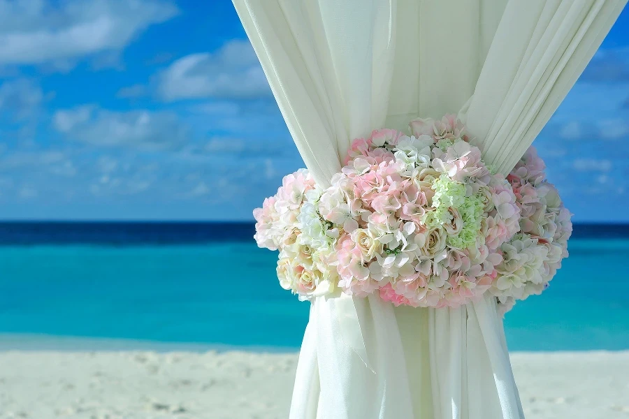 Flowers wrapped around a white curtain on a beach