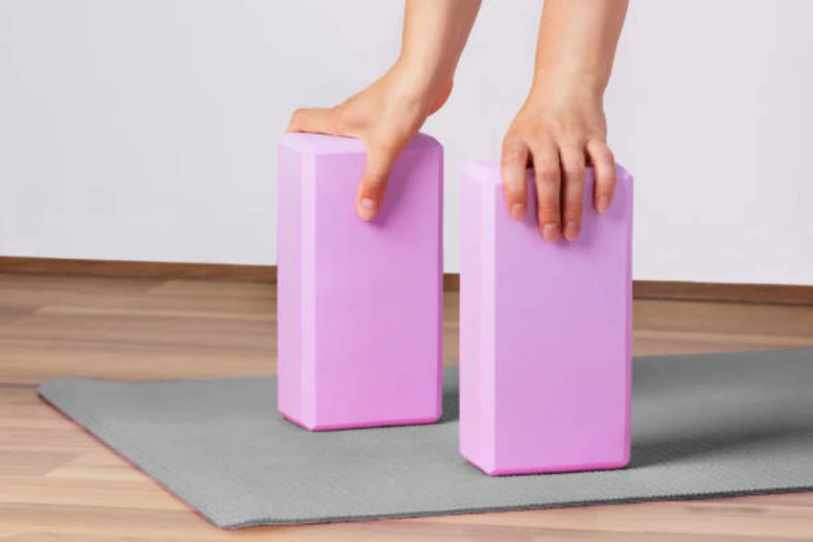 Hands holding one purple yoga block each on yoga mat
