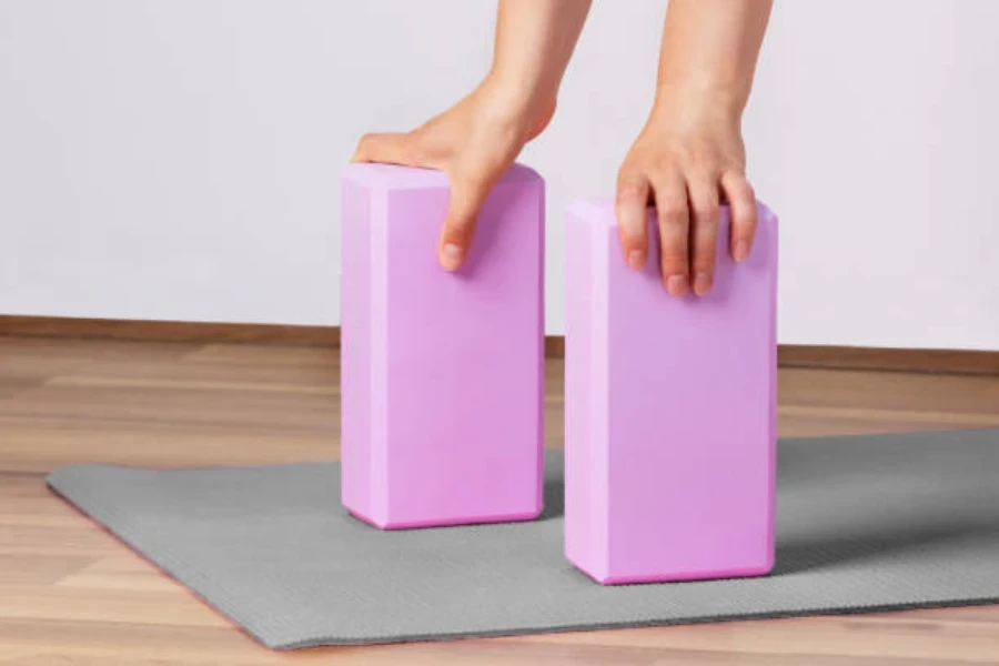 Mains tenant chacune un bloc de yoga violet sur un tapis de yoga