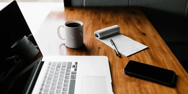 Laptop, cup of coffee, smartphone and notepad sitting on a wooden table