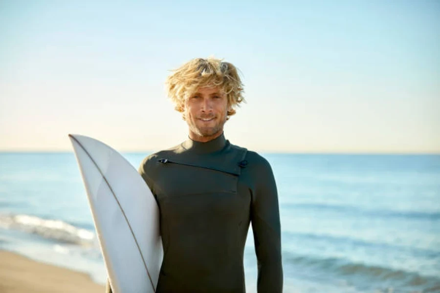 Surfista masculino sosteniendo una tabla y vistiendo un traje de neopreno negro