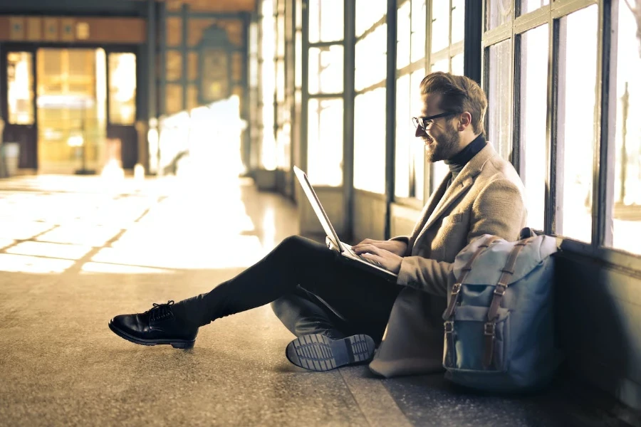 Un uomo in giacca e cravatta aspetta all'aeroporto con un laptop in equilibrio sulle ginocchia