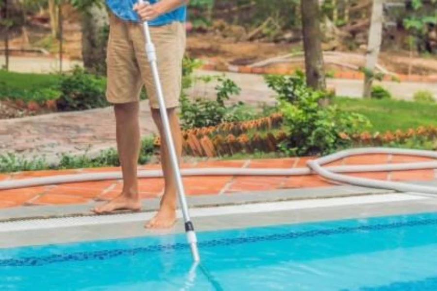 Hombre en pantalones cortos usando un poste telescópico para limpiar la piscina