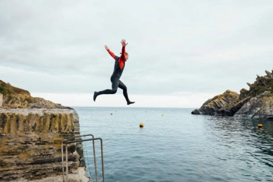 Man jumping in open water wearing red and black wetsuit