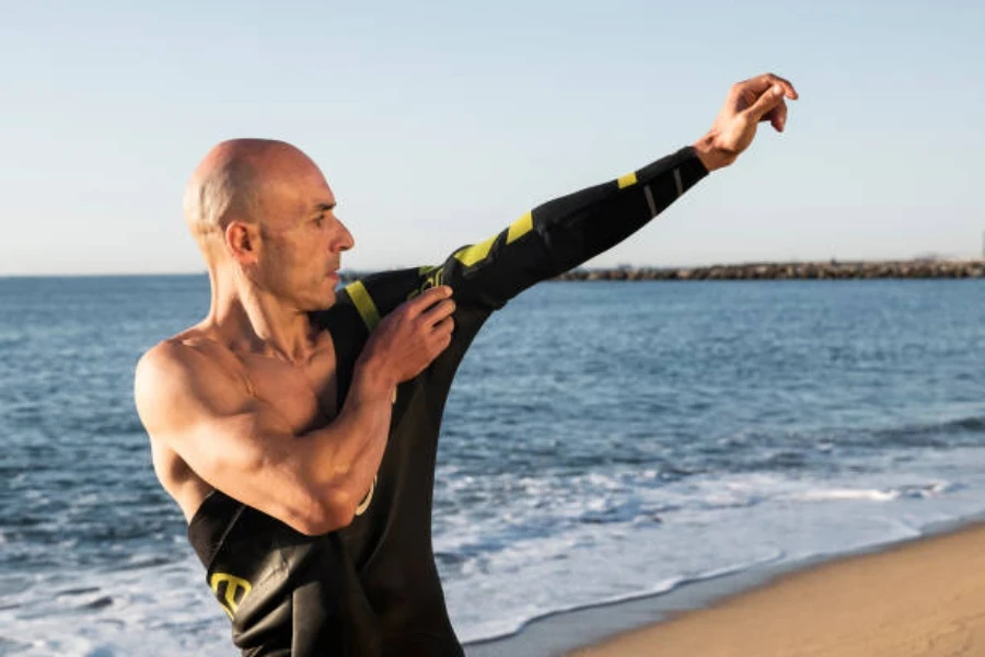 Man pulling on black wetsuit next to the ocean