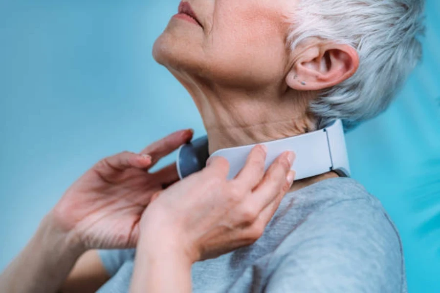 Mulher mais velha usando massageador de pescoço cinza para aliviar a dor