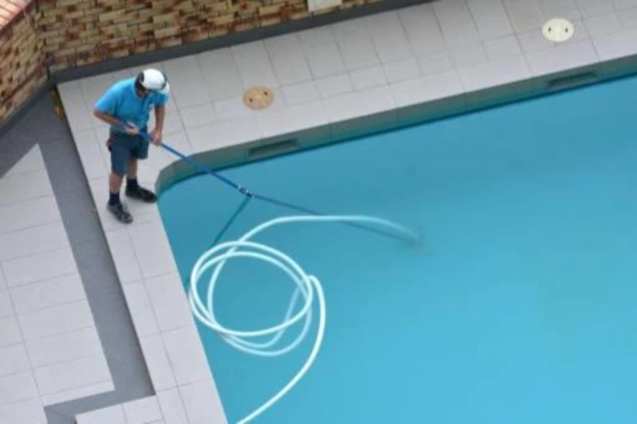 Person reinigt Pool mit Saugkopf und Schlauch