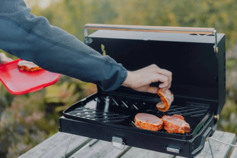 person placing raw meat on outdoor electric grill for camping