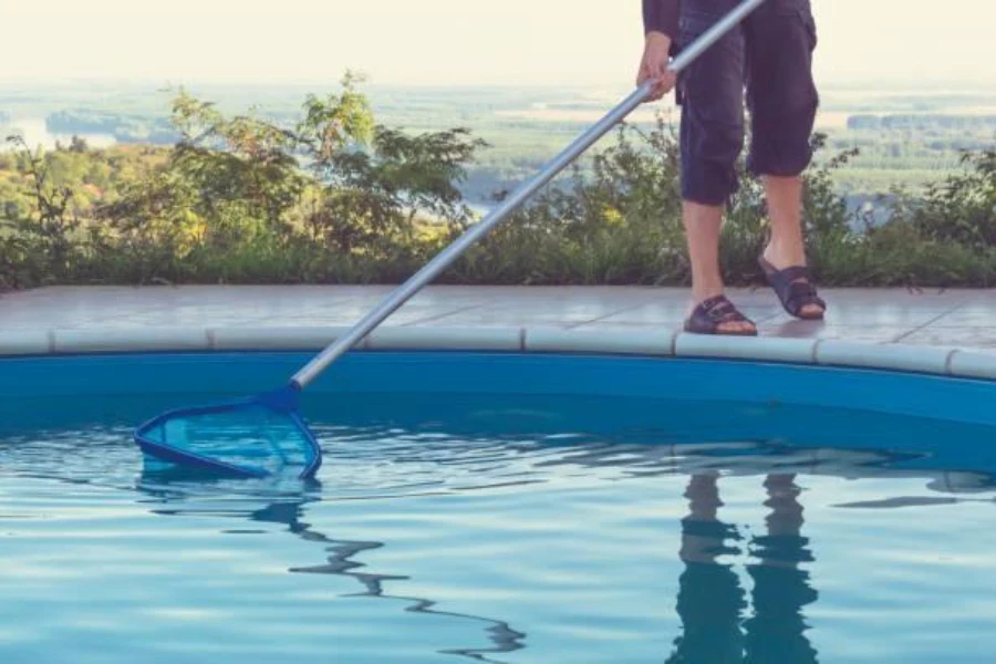 Persona que utiliza una red skimmer para filtrar la suciedad de la piscina