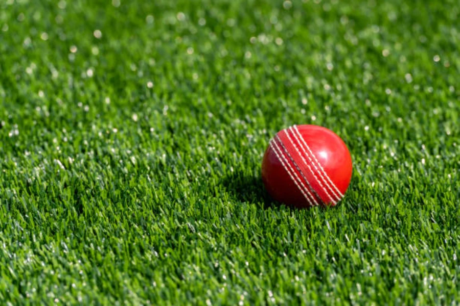 Red cricket ball sitting on short artificial grass outdoors