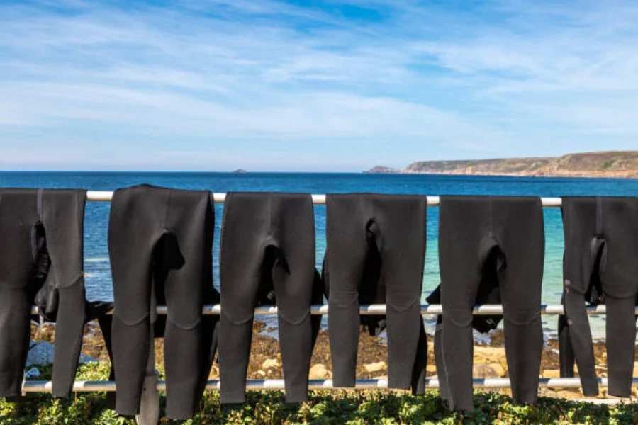 Row of black cold water wetsuits hung up on railing