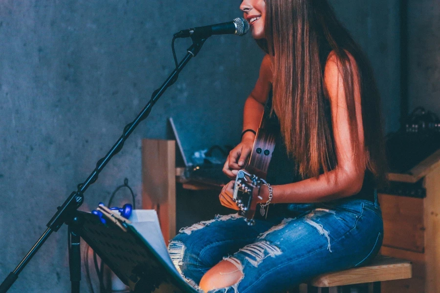 Mulher sentada tocando violão enquanto canta para o suporte do microfone