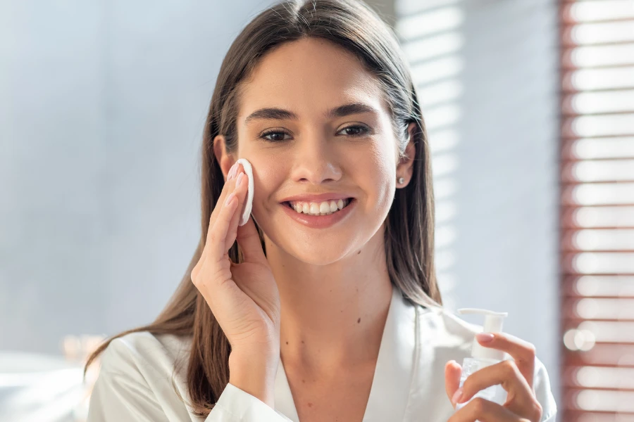 Smiling woman holding serum and using facial cotton pads