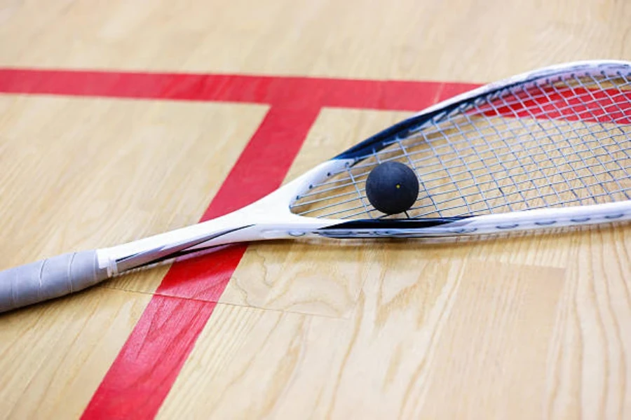 Raqueta de squash y pelota de squash sentada en una cancha cubierta de madera