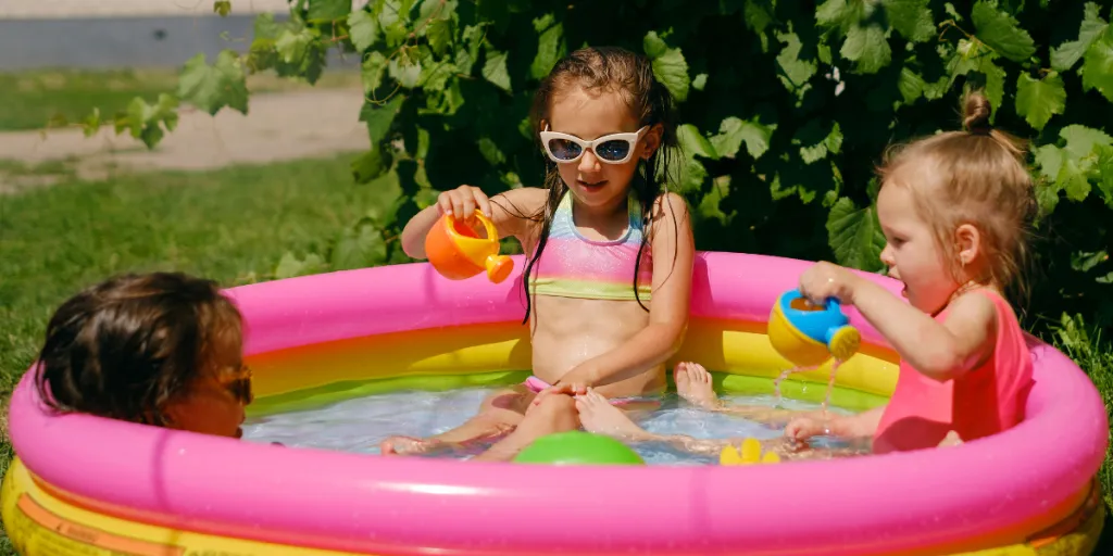 Three children playing with toys in a pink inflatable pool
