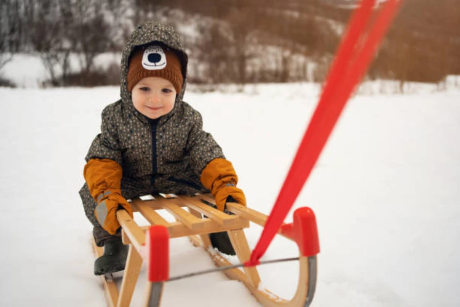 Toddler being pulled on small wooden sled in snow