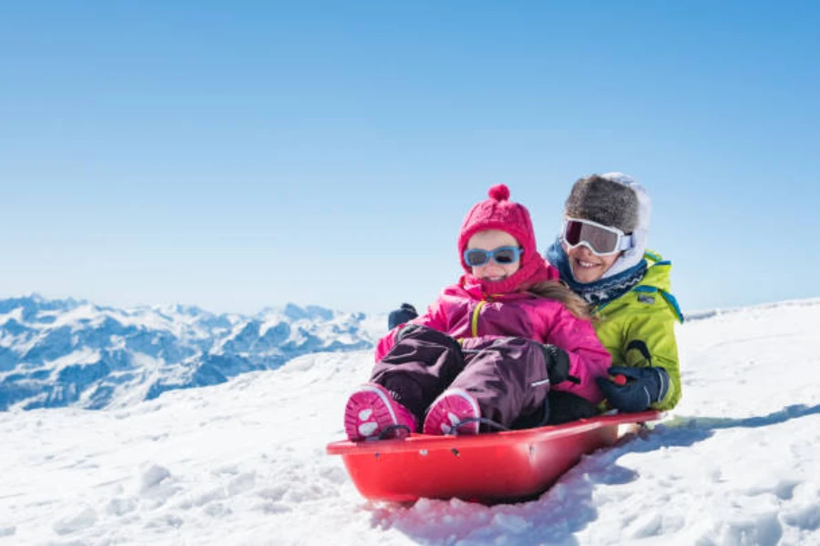 Two children sitting on red sled going down snowy hill