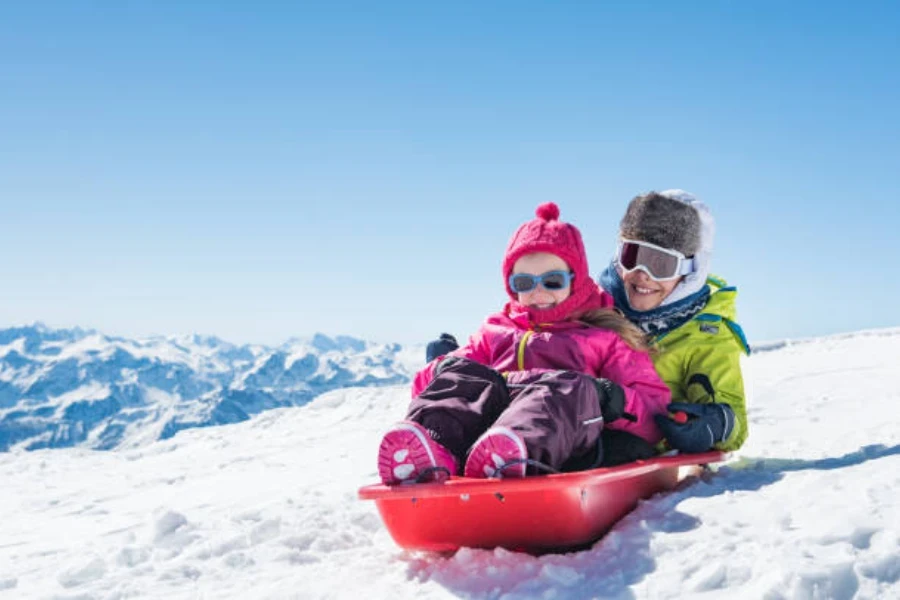 Deux enfants assis sur un traîneau rouge descendant une colline enneigée