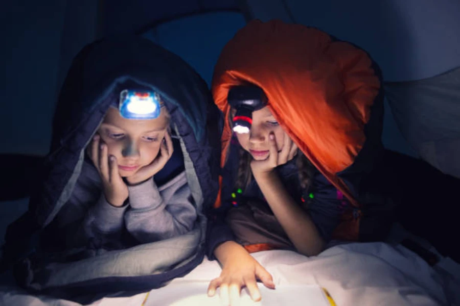 Two children wearing camping headlamps while reading in tent