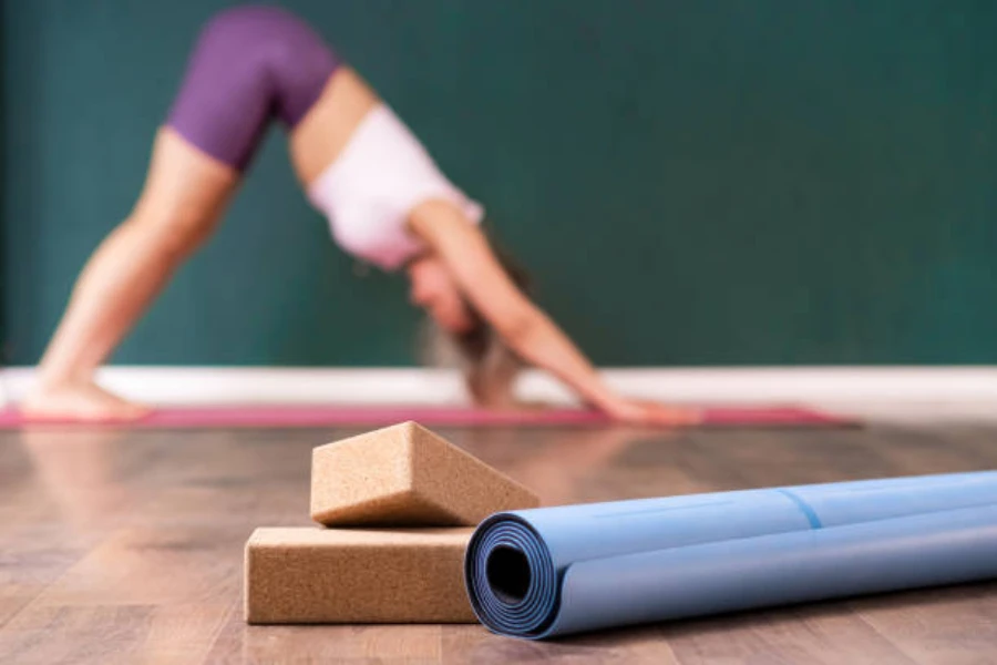 Two cork yoga blocks piled next to blue yoga mat