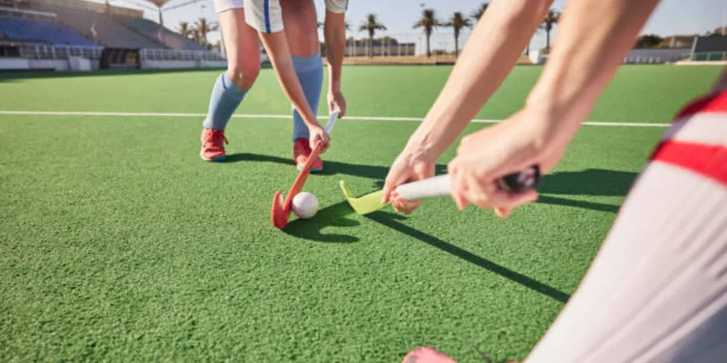 Two people playing field hockey on artificial grass outdoors