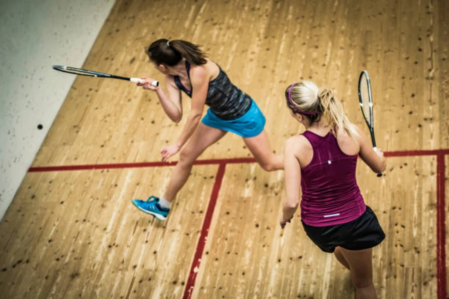 Two women playing squash indoors on wooden floor