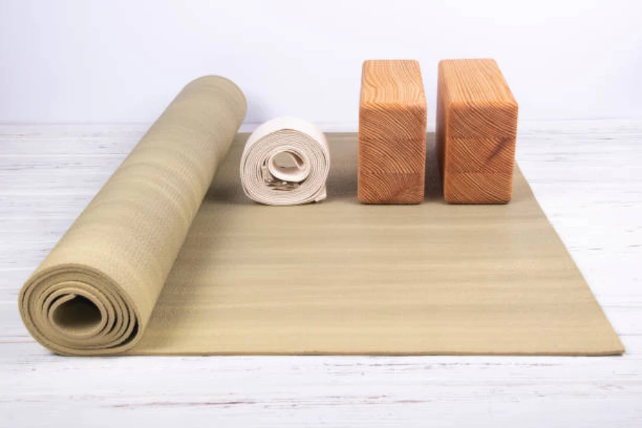 Two wooden yoga blocks on yoga mat with rolled straps