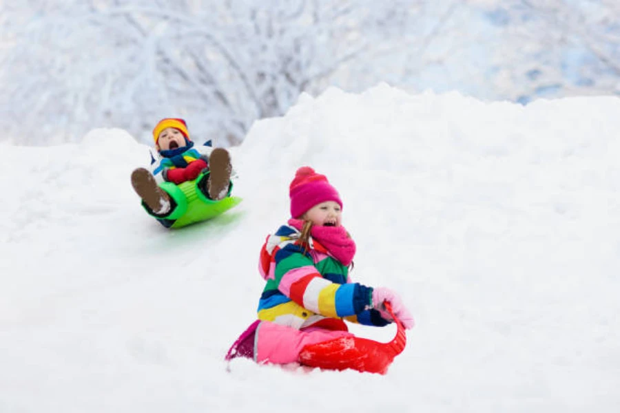 Two young children going downhill on plastic snow sleds