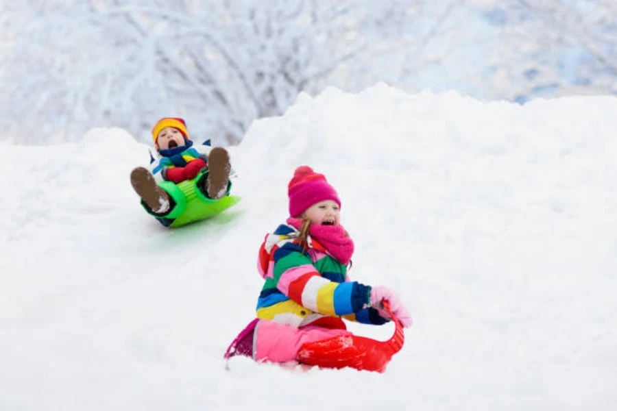 プラスチック製の雪そりで下り坂を行く XNUMX 人の幼い子供