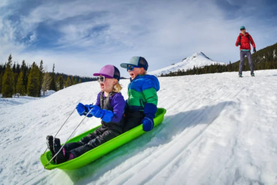 Two young children on long green plastic sled in winter