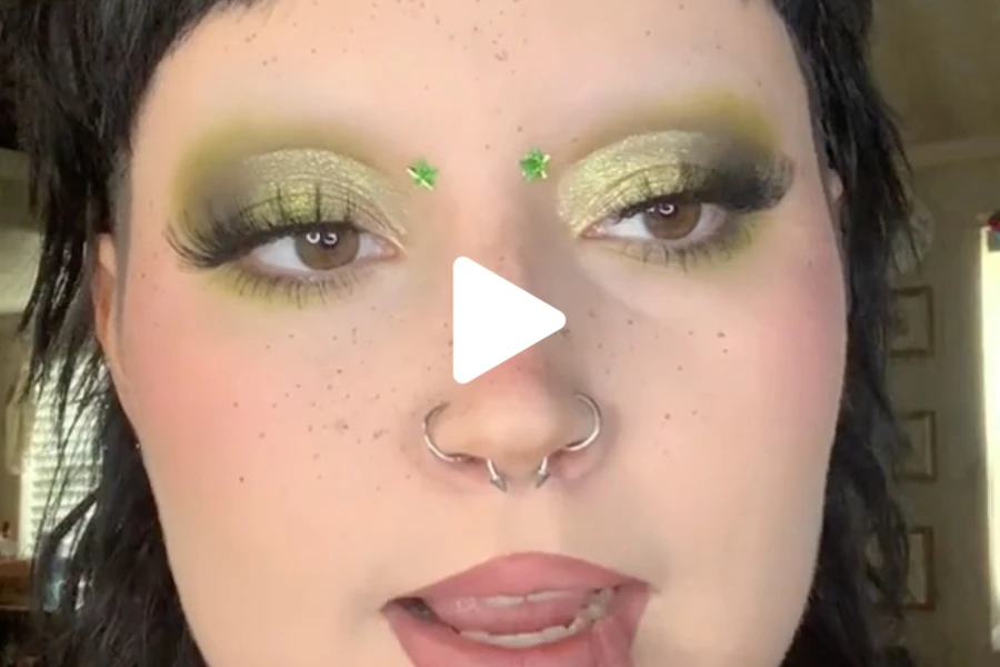 Woman applying makeup with no eyebrows and green eyeshadow