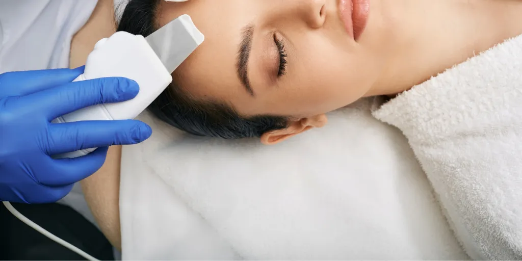 Woman being treated with an ultrasonic skin scrubber by esthetician