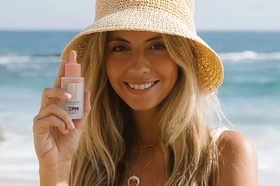 Femme tenant des gouttes bronzantes sur la plage