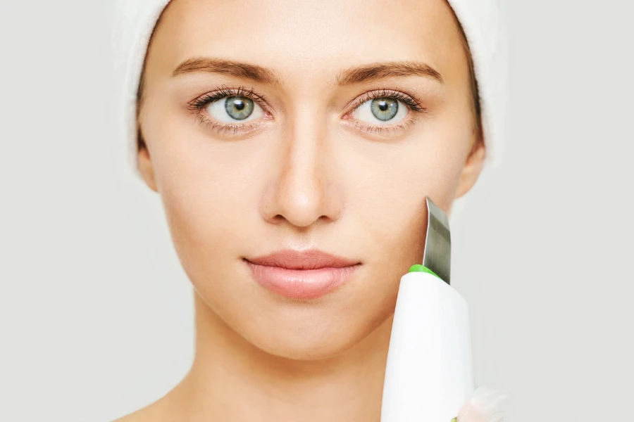 Woman holding white wireless ultrasonic skin scrubber against her cheek