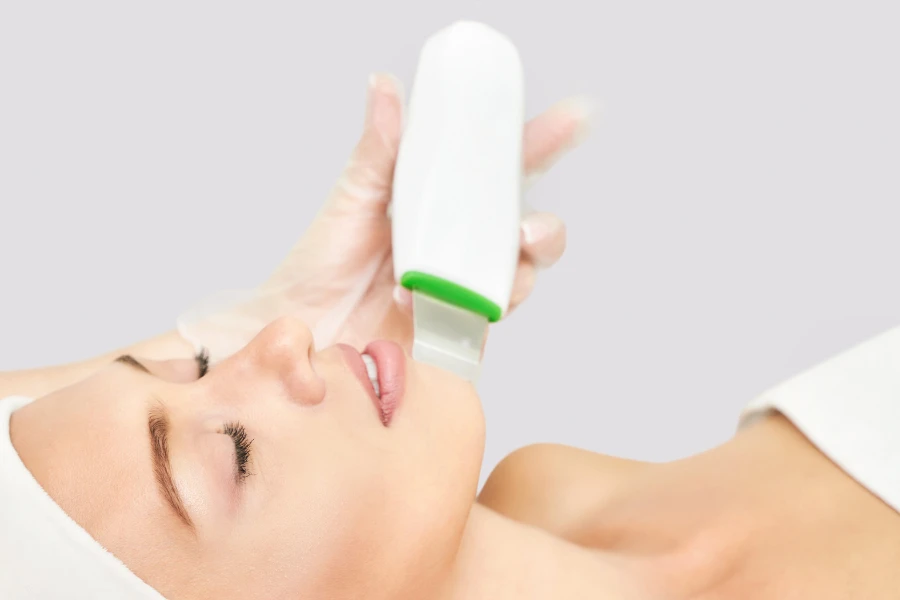 Woman lying down while esthetician uses wireless ultrasonic skin scrubber