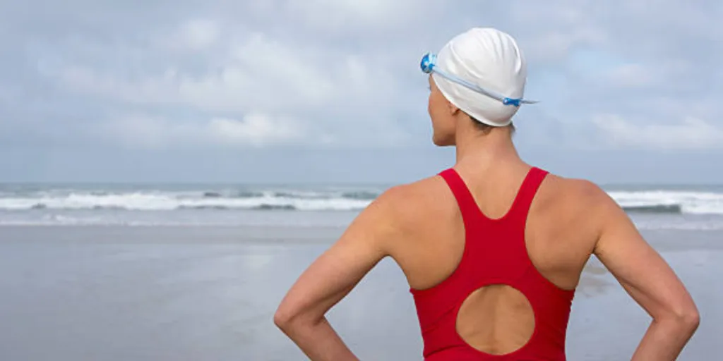 Woman standing on beach wearing white swimming cap