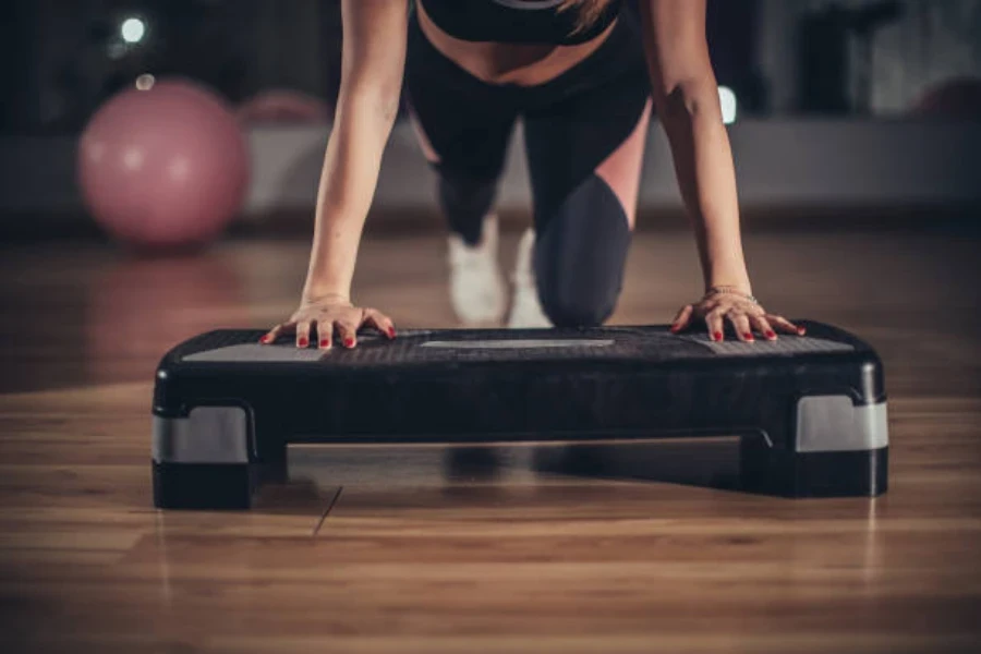 Mujer usando plataforma de ejercicio escalonada negra y gris para abdominales