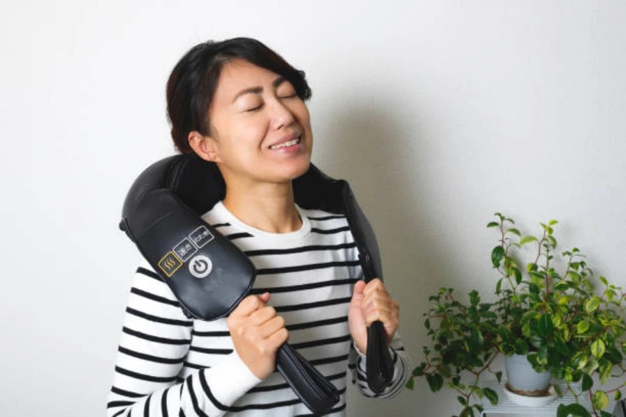 Woman using long black neck and shoulder massager at home