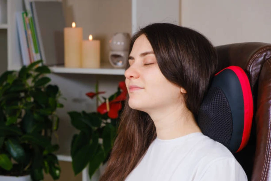 Woman using pillow neck massager at home on chair