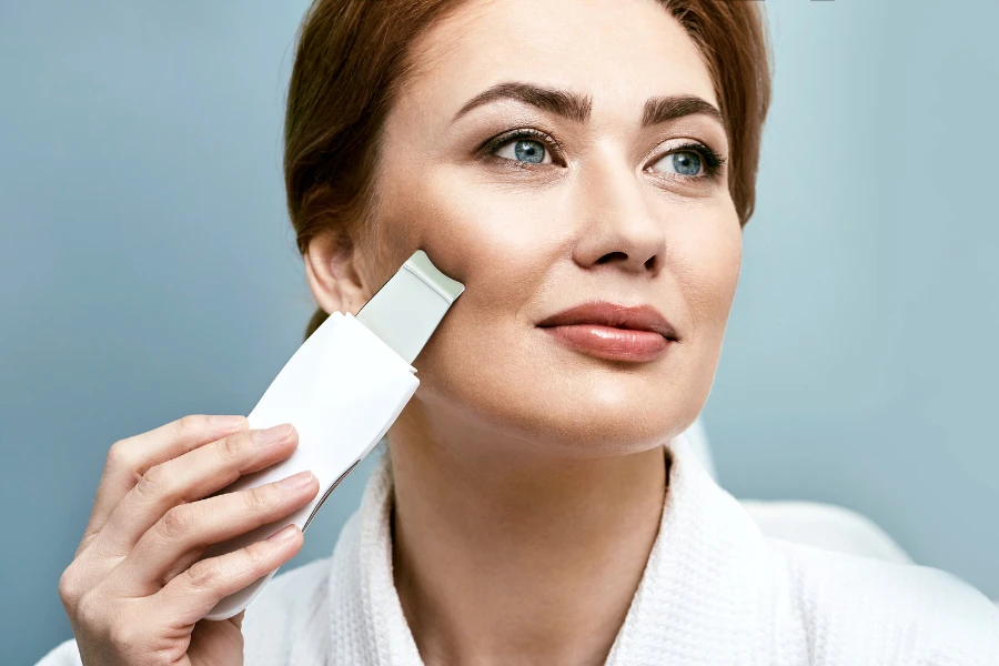 Woman using white wireless ultrasonic skin scrubber on her face