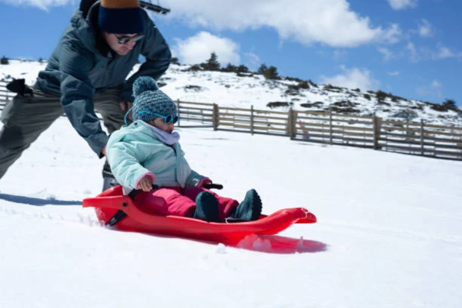 Young girl being used downhill sitting in red plastic sled