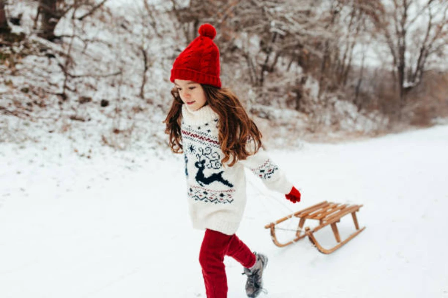 Young girl pulling small wooden sled through the snow