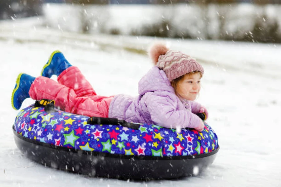 Young girl sliding downhill in colorful inflatable sled