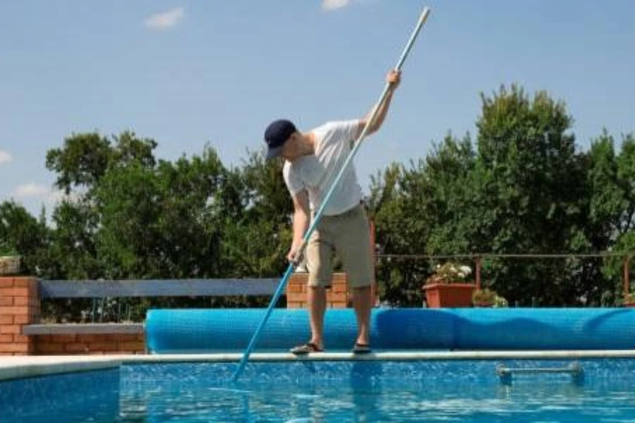 Young man using a telescopic pole to clean pool