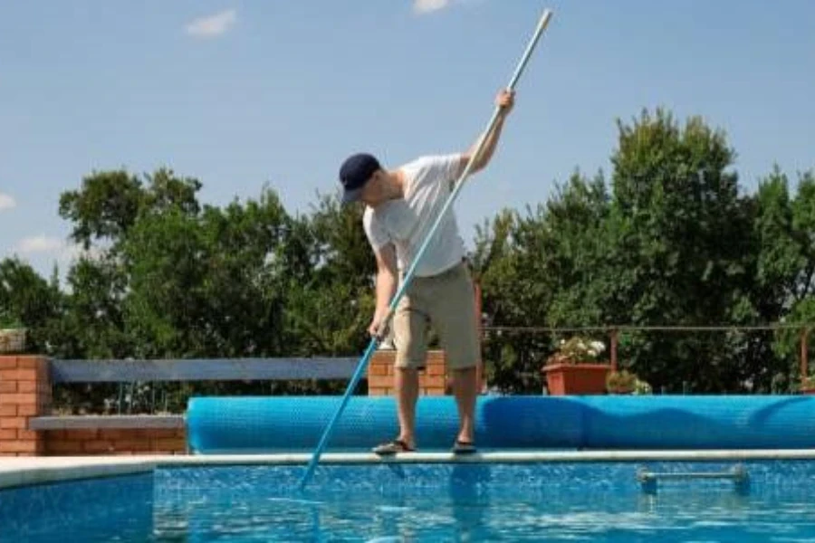 Junger Mann benutzt eine Teleskopstange, um den Pool zu reinigen