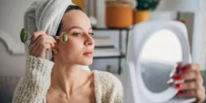 Young woman using a jade roller while using a mirror