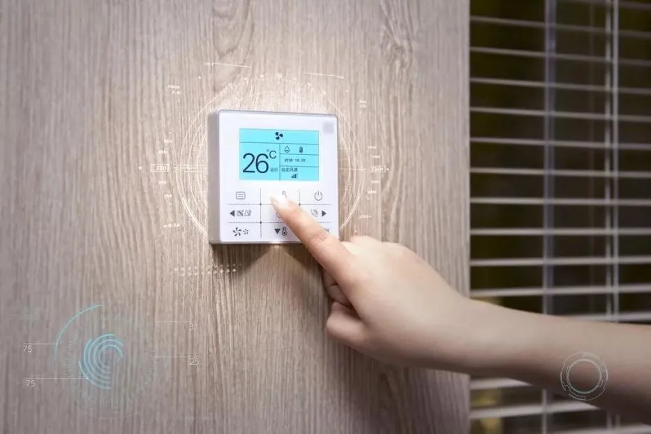 A person's finger adjusting a modern smart thermostat mounted on a wooden wall