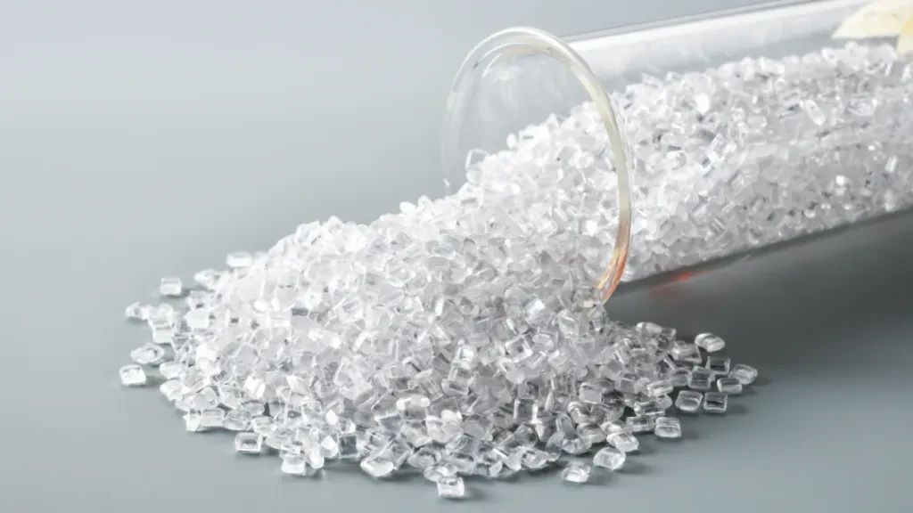 Granules de polycarbonate transparent s'échappant d'un tube à essai en verre sur une surface grise